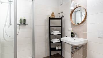 Une salle de bain moderne avec une douche à parois de verre, un lavabo blanc avec un miroir et une étagère noire où sont posées des serviettes.