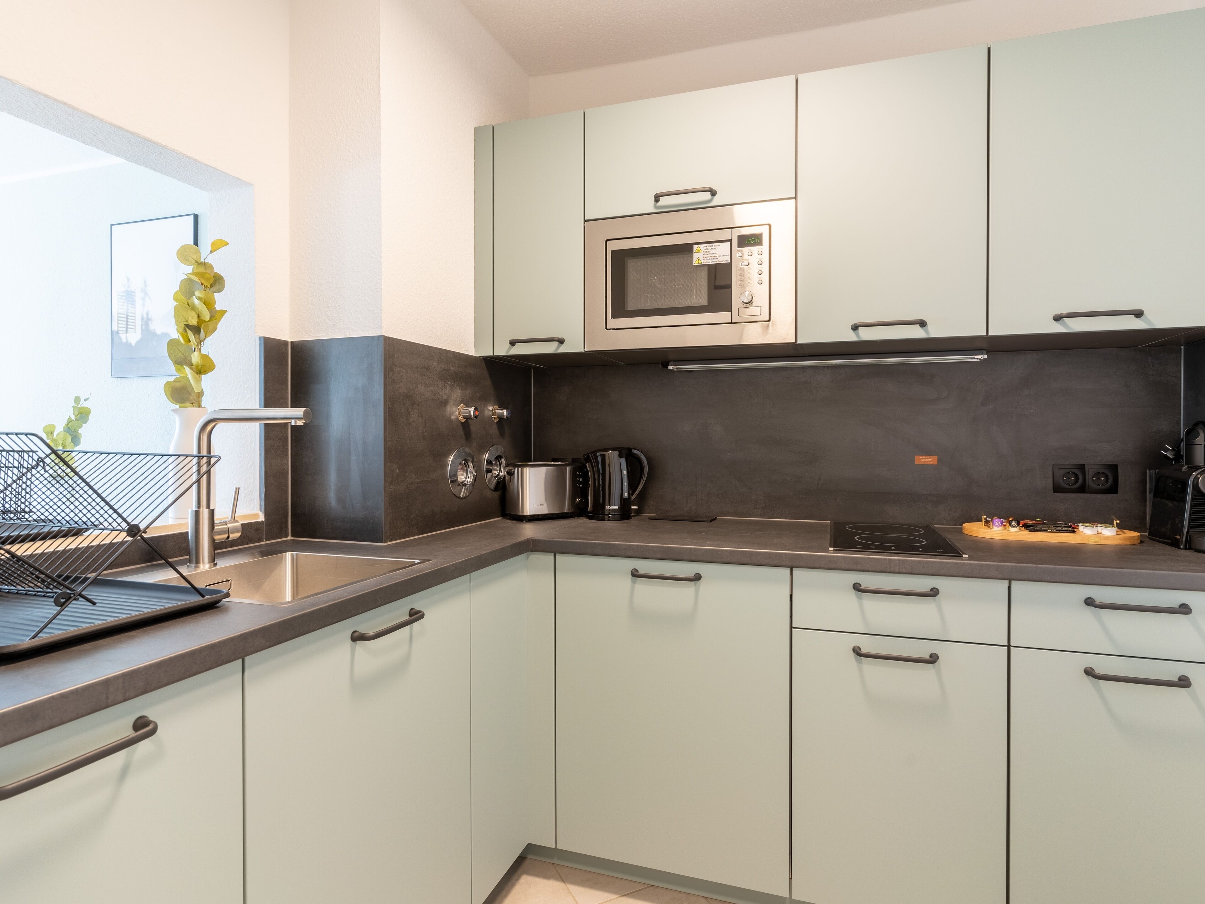 A modern kitchen with light-colored cabinets, a stainless steel microwave, a kettle, and a coffee machine.