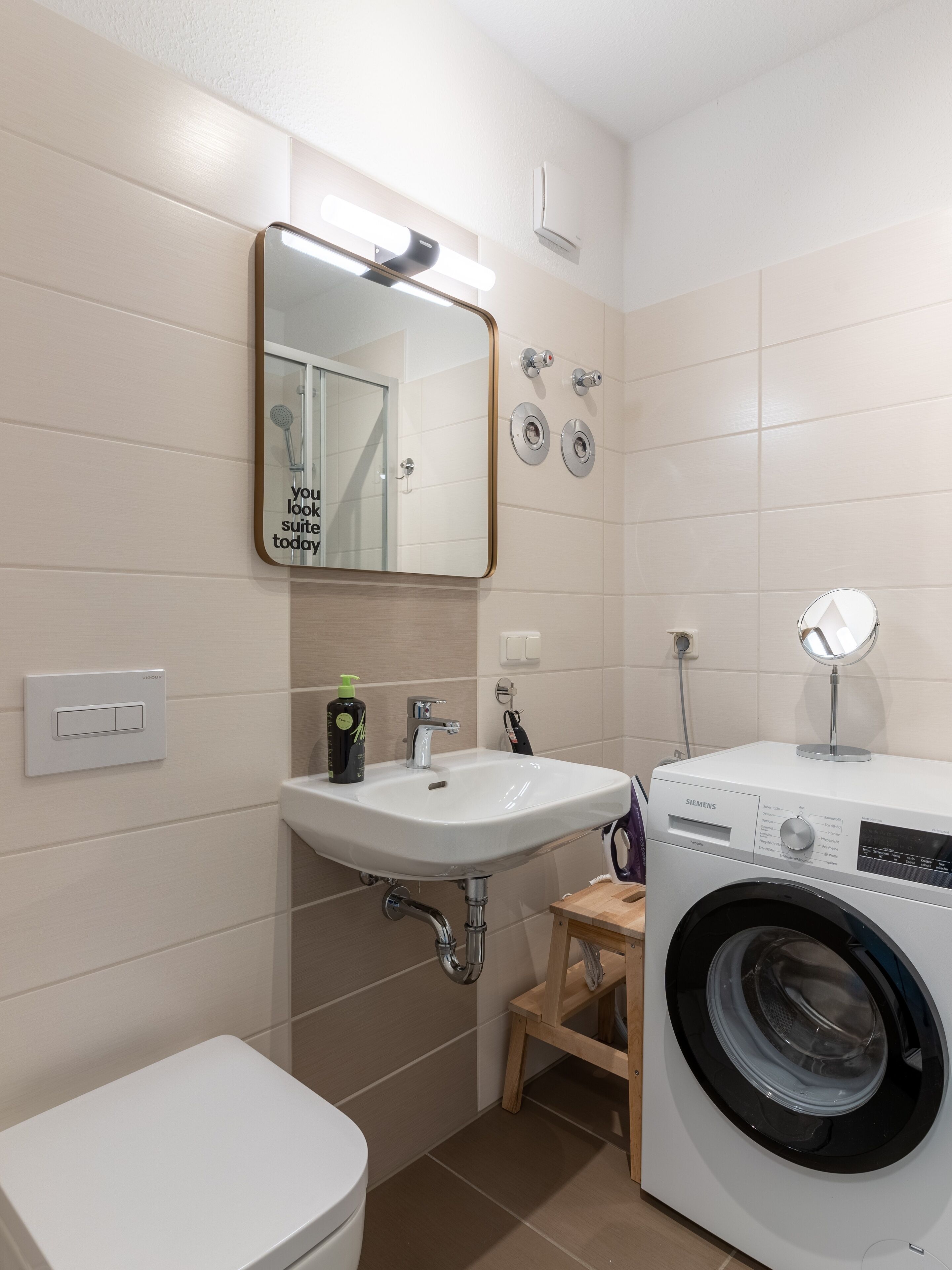 A modern bathroom with a white sink, mirror, and a built-in washing machine.