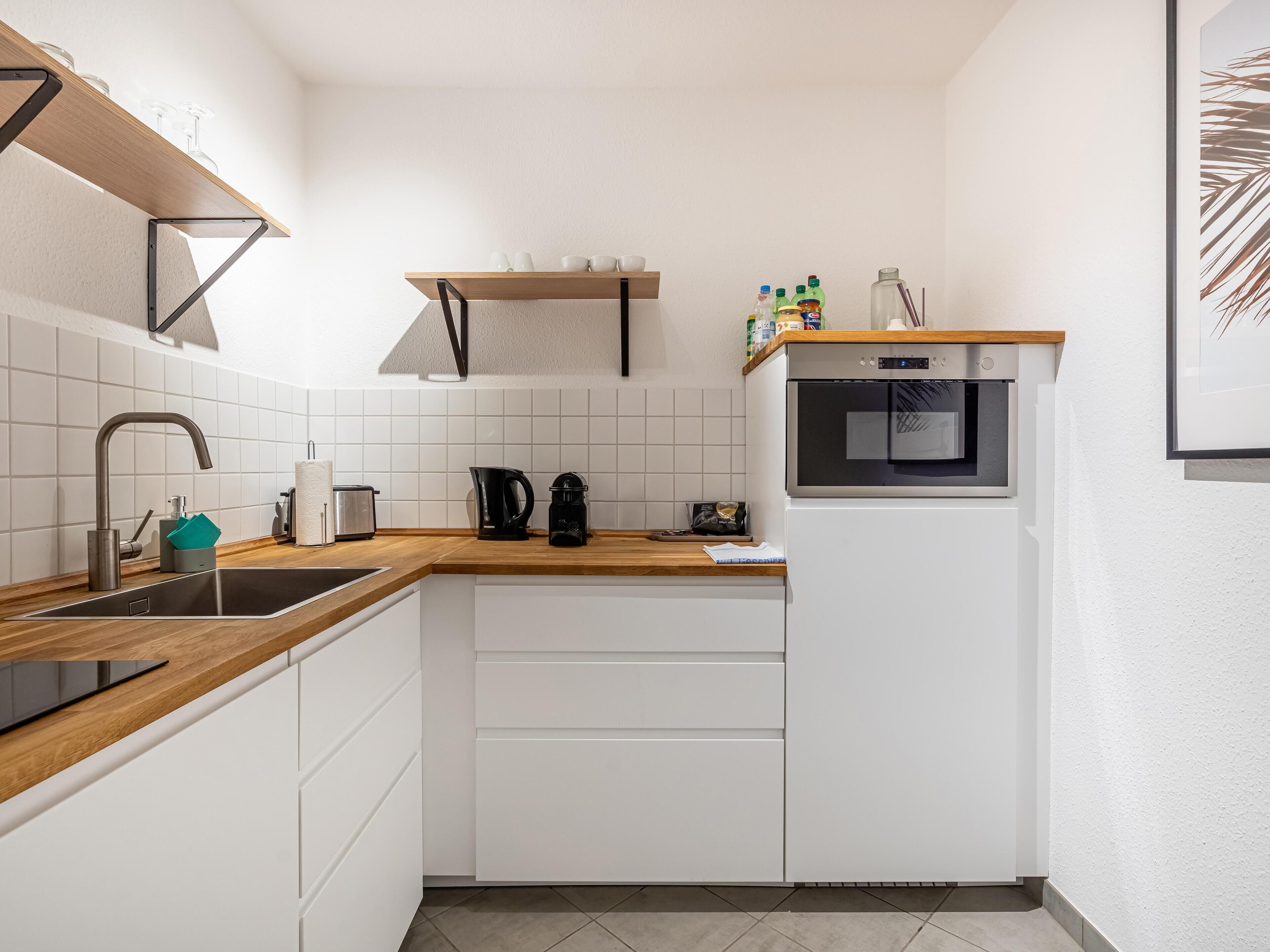 Eine moderne Küche mit weißen Schränken, einer Holzauskładung, einer Edelstahlspüle, einer Kaffeemaschine und einem eingebauten Ofen.