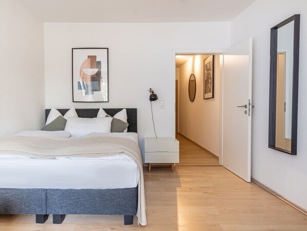 A modern bedroom with a bed, bedside table, and a hallway leading to another room. - Limehome Magdeburg Hasselbachplatz (Magdeburg)