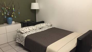 Un dormitorio ordenado con cama, mesitas de noche, una lámpara y un florero con adornos.