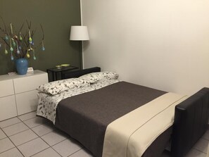 A neatly arranged bedroom with a bed, bedside tables, a lamp, and a vase with decorative balls.
