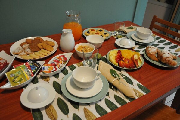 Una mesa de desayuno con platos de pasteles, frutas y una jarra de zumo de naranja.