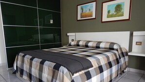 Un dormitorio moderno con una cama grande, un armario de puertas de cristal y dos cuadros de paisajes en la pared.