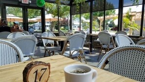 Un espacio al aire libre con sillas y mesas de mimbre, un letrero de madera con un número y una taza blanca.