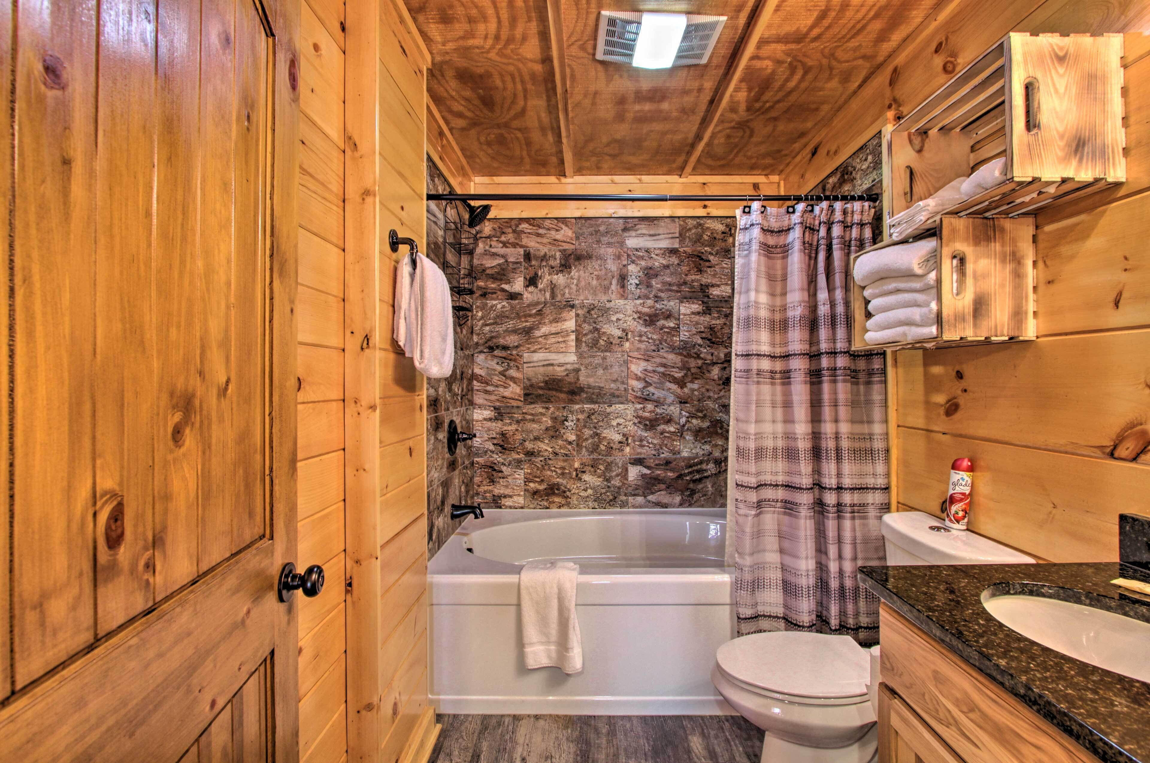 A wooden cabin bathroom with a stone wall, a bathtub, a toilet, and a sink.