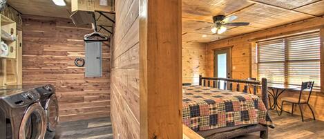 Interior de una cabaña de madera con una cama, una mesa y un ventilador de techo.