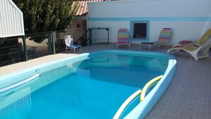 En swimmingpool med ett kaklat poolområde, solstolar och ett inhägnat område med en grind.
