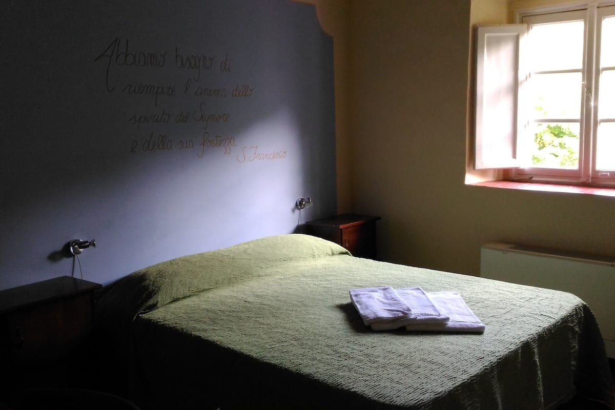 Un dormitori amb un llit, una tauleta de nit, una làmpada, una finestra i una paret amb text.