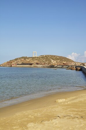 A coastal scene with a sandy beach, a rocky hill, and a structure with a white frame on top.