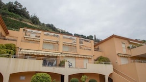 A multi-story building with balconies, a covered walkway, and small landscaped areas. - Cozy 2BR with terrace, pool, and garage (Menton)