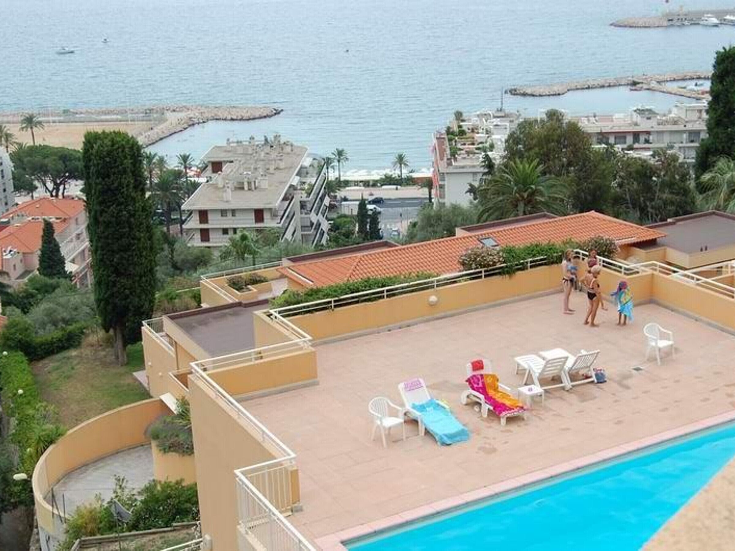 A rooftop pool area with lounge chairs and a view of the sea and buildings.