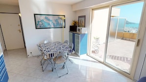A dining area with a table and chairs, a microwave, and a view of the sea through a sliding glass door. - Cozy 2BR with terrace, pool, and garage (Menton)