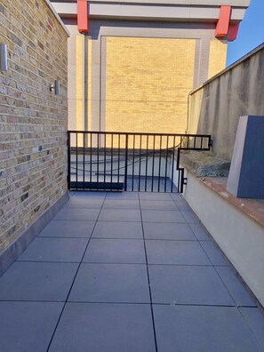 A courtyard with tiled flooring, a brick wall, and a metal gate. - Stylish Maisonette and studio in Victoria (London)