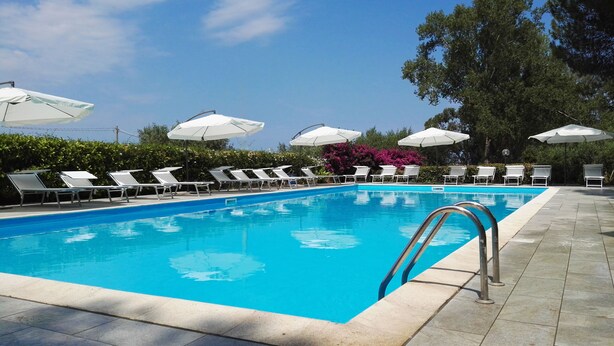 A swimming pool with lounge chairs and umbrellas, surrounded by greenery. - Sweet Home La Conturella (Ricadi)