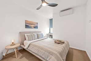 A bedroom with a bed, bedside table, lamp, ceiling fan, and a painting on the wall. - Chic 2 bed / 2 bath Apartment with City Views (Teneriffe)