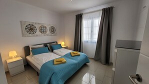 A bedroom with a bed, nightstands, a lamp, a window with curtains, and a refrigerator. - Beautiful apartment with stunning views and communal pool (Puerto del Carmen)