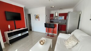A modern living room with a red accent wall, a flat-screen TV, a white sofa, and a coffee table with decorative items. - Beautiful apartment with stunning views and communal pool (Puerto del Carmen)