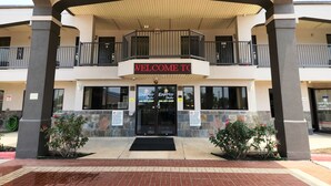 A hotel entrance with a 'WELCOME TO' sign, a covered entrance area, and a two-story building with balconies.