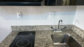 A kitchen with a black induction cooktop, a stainless steel sink, and granite countertops.