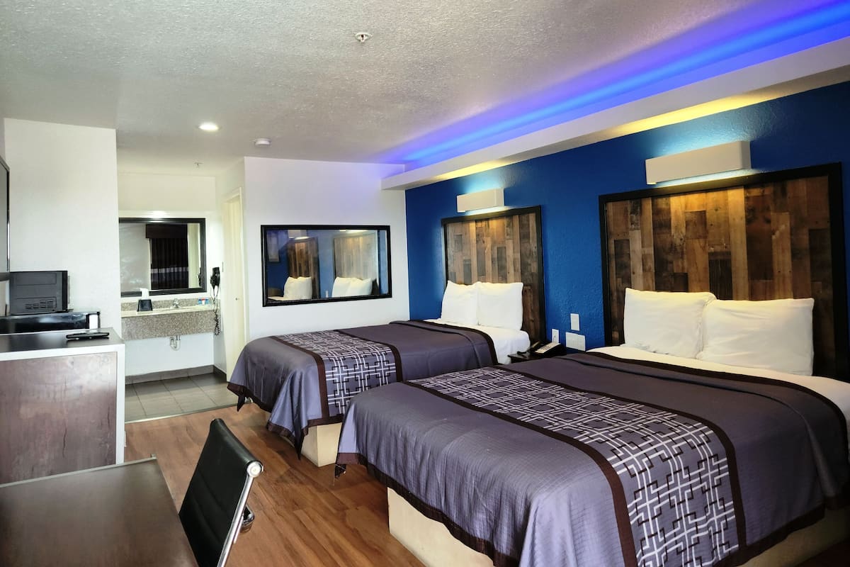 A hotel room with two beds, a small kitchenette, a mirror, and a wooden headboard.
