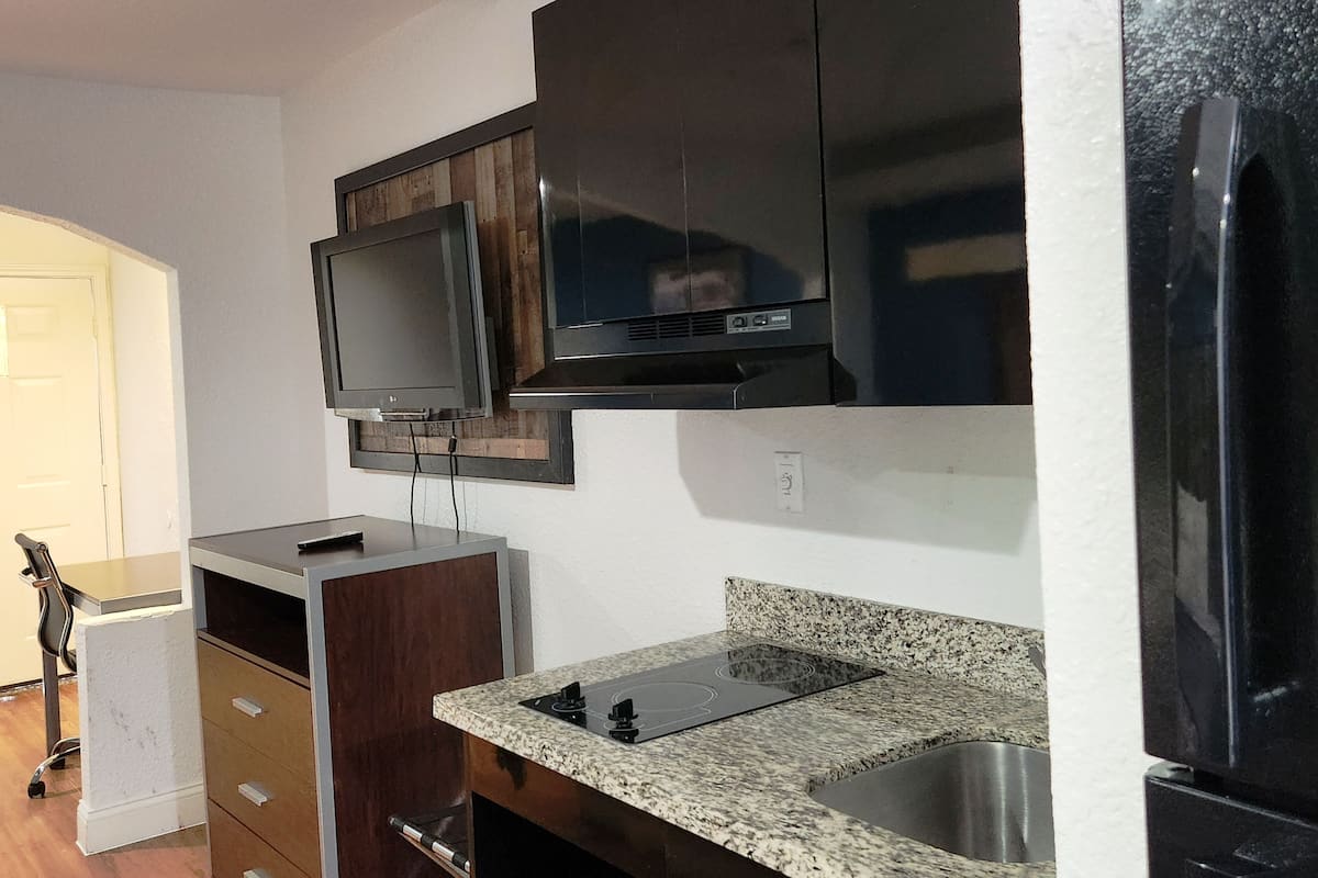 A kitchen with dark wooden cabinets, a built-in microwave, a stainless steel sink, and a black refrigerator.