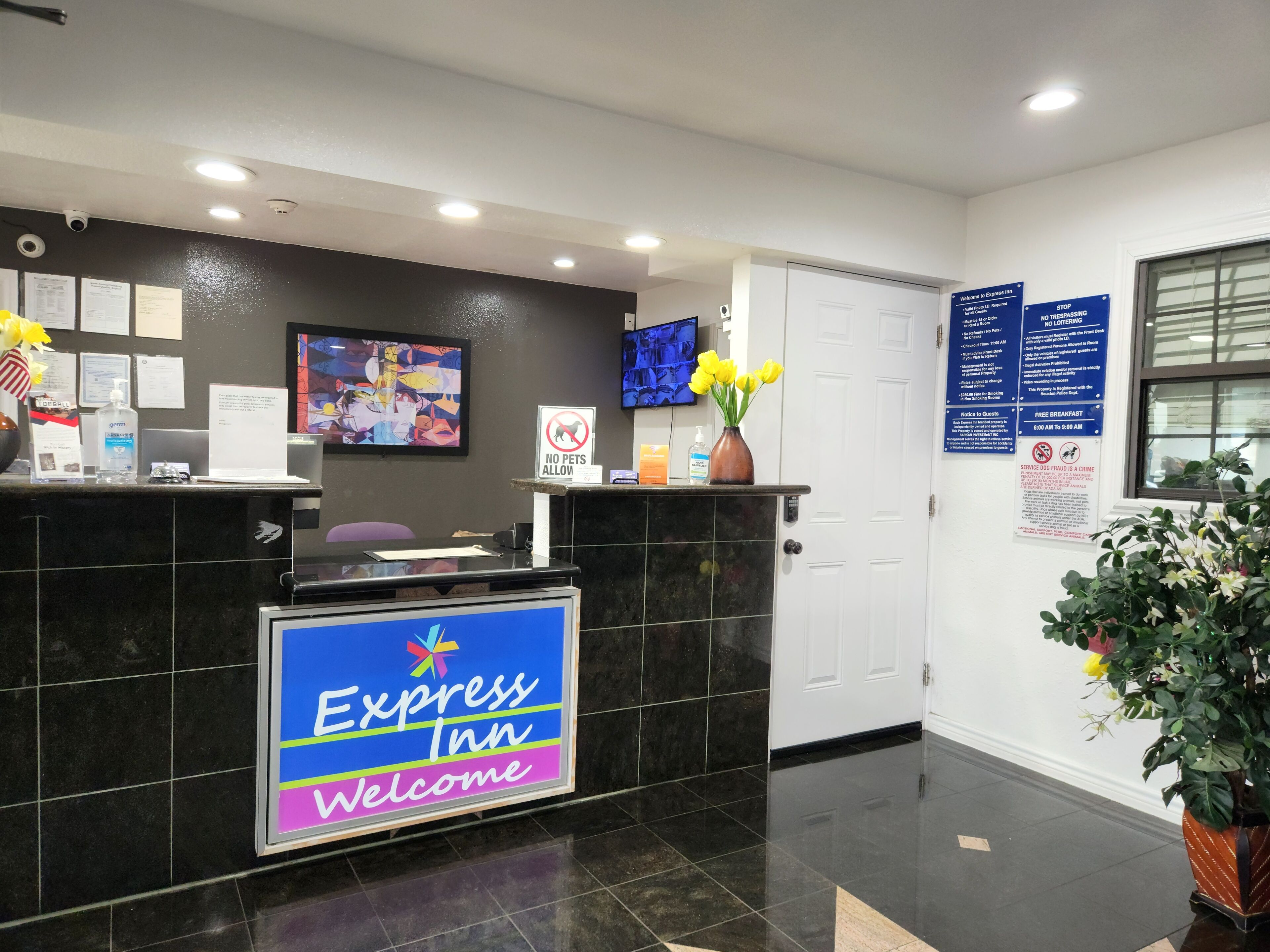 Zona de recepción de hotel con mostrador de mármol negro, un cartel de 'Bienvenido' y carteles informativos en la pared.