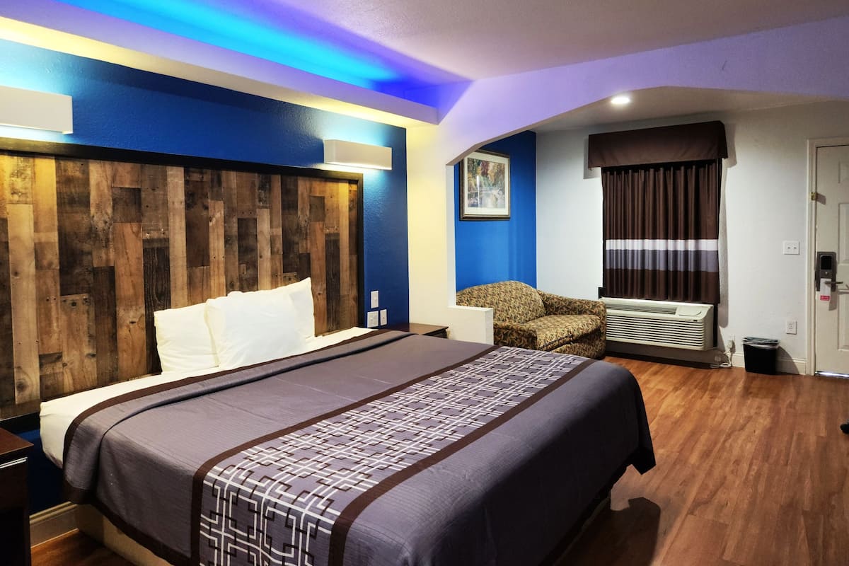 A hotel room with a large bed, a wooden headboard, a sofa, an air conditioning unit, and a door with a striped curtain.