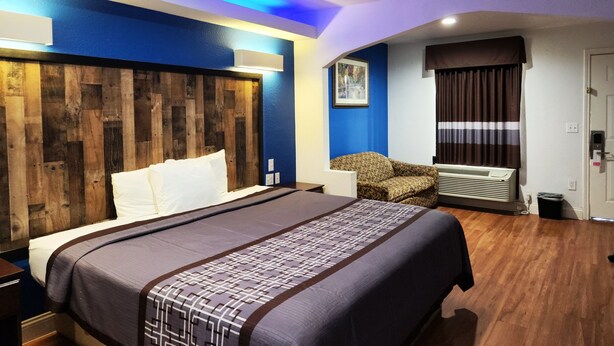 A hotel room with a large bed, a wooden headboard, a sofa, an air conditioning unit, and a door with a striped curtain.
