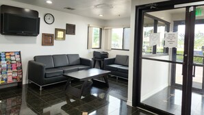 A modern waiting area with a black leather sofa, a coffee table, and a television mounted on the wall.
