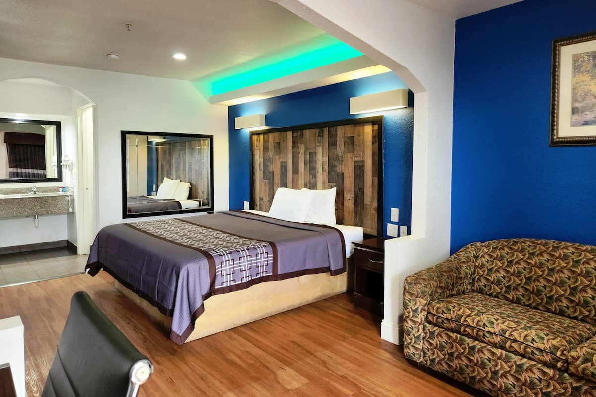 A hotel room with a bed, a sofa, a desk, and a mirror.