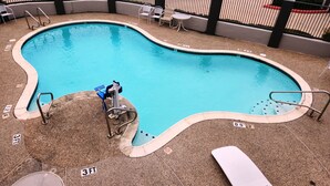 A swimming pool with a diving board, lounge chairs, and a fenced area with chairs.