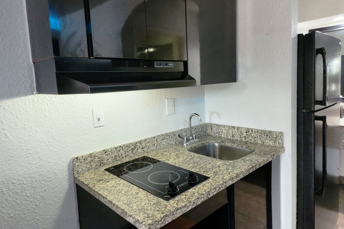 A compact kitchen with a granite countertop, a built-in stove, a sink, and a black range hood above the stove.