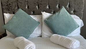 Ein ordentlich bezogenes Bett mit weißen Leinen und zwei türkisfarbenen Kissen.
