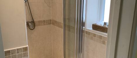 Eine Dusche mit Glastür, eine Toilette und ein kleines Fenster mit Korb auf der Fensterbank.