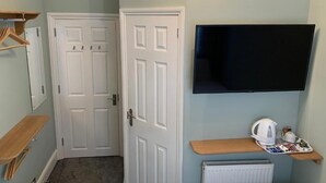 Ein Zimmer mit weißer Tür, einem an der Wand montierten Fernseher, einer Heizung und einem Tablett mit Wasserkocher und Tassen.