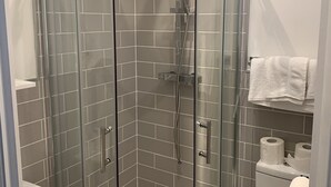 Ein Duschbereich mit Glaswand, einer Handbrause, einem weißen Waschbecken und einer Toilette mit Handtuchhalter.