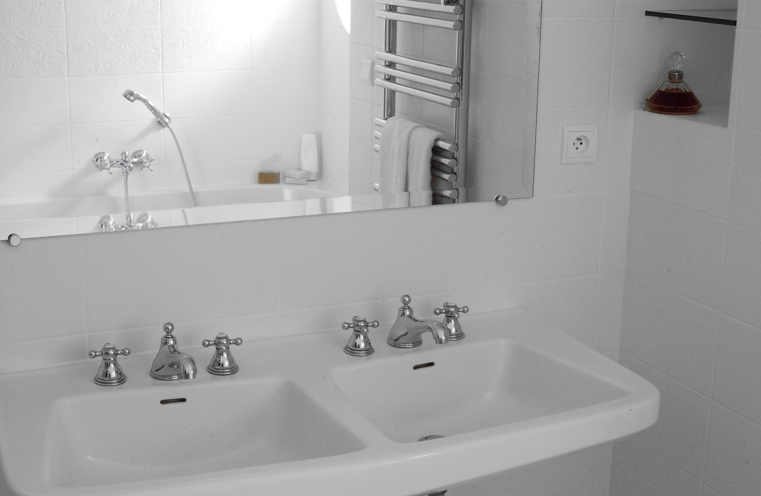 A bathroom with a white sink, two faucets, a mirror, and a towel rack.