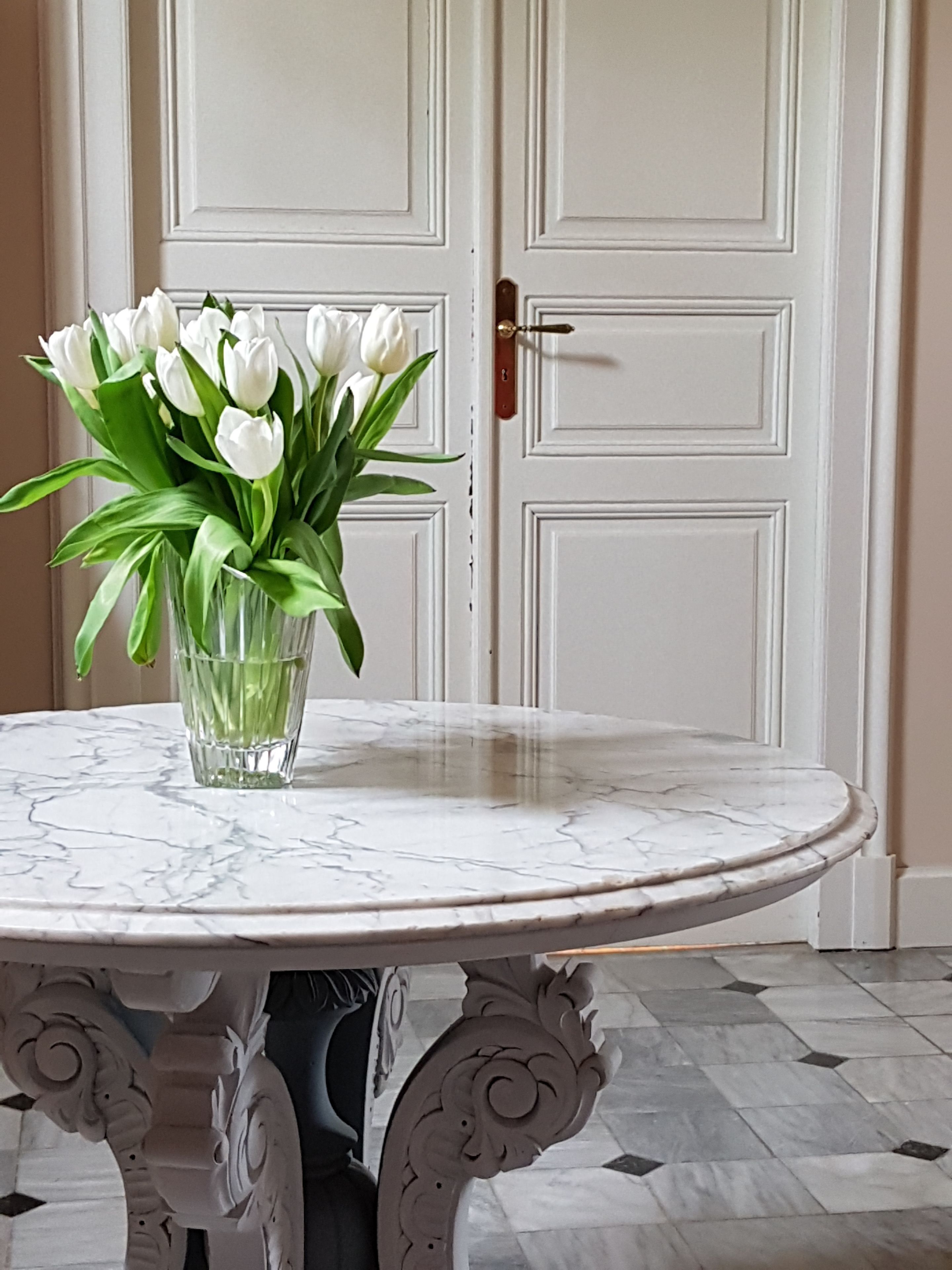 A round marble table with a glass vase of white tulips.