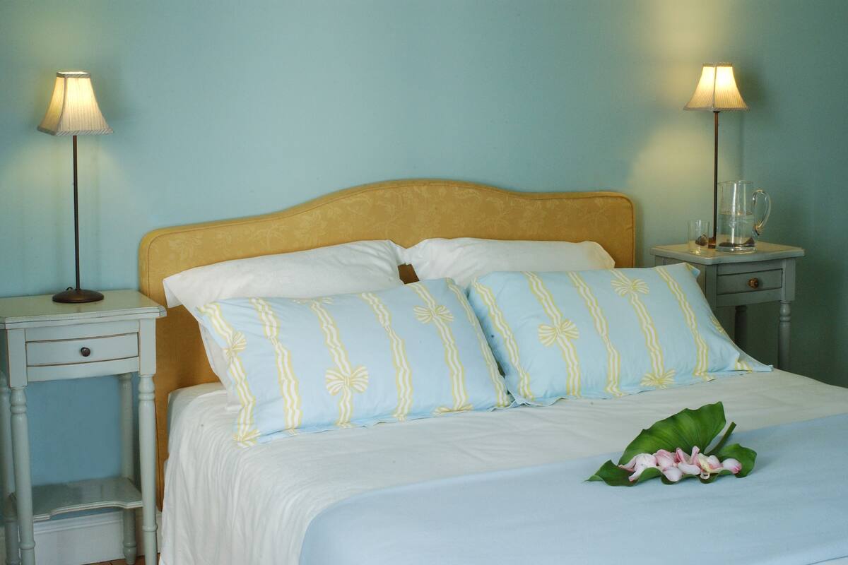 A bed with white and light blue striped pillows, a wooden headboard, and a bedside table with a lamp.