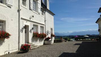 A white building with a gravel courtyard, red flower boxes, and a view of mountains in the background.