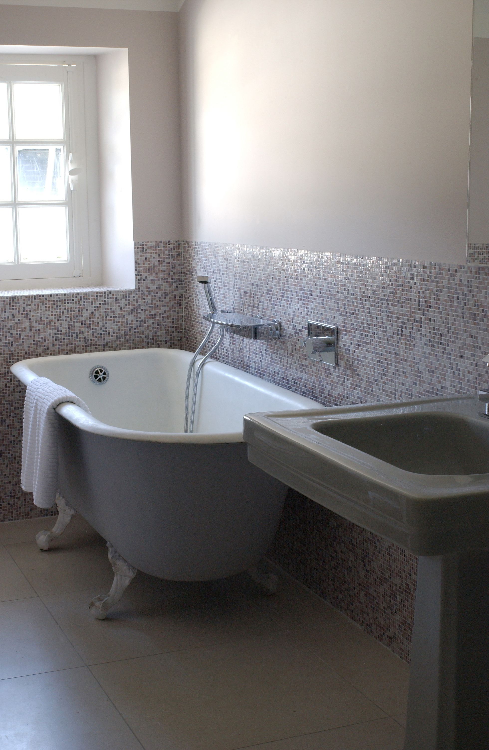 A bathroom with a clawfoot bathtub, a sink, and a window.
