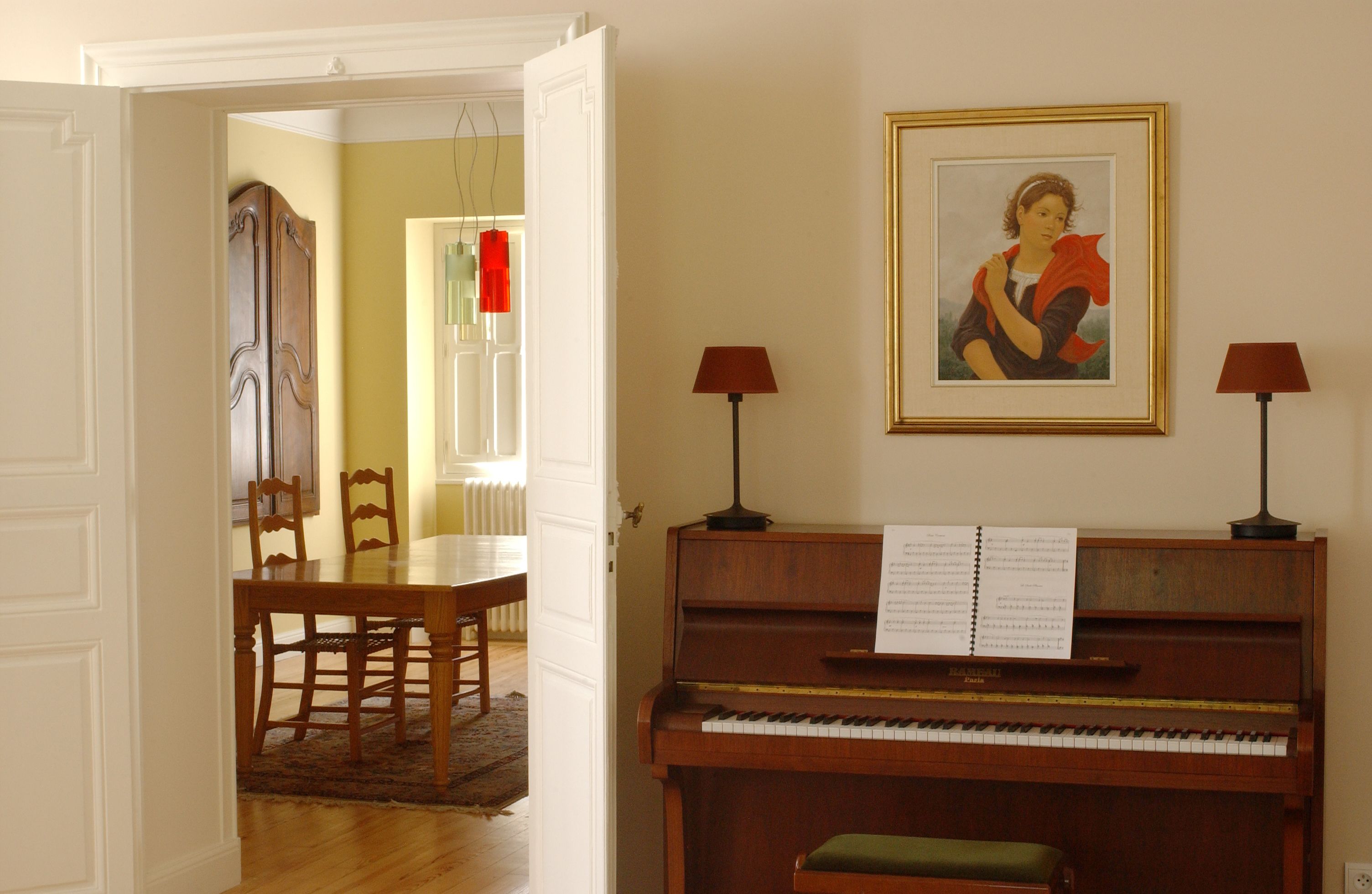 Puerta abierta que da a un comedor con un piano y un cuadro en la pared.