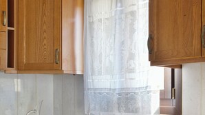 A kitchen with wooden cabinets, a sink, and a window with a lace curtain. - Two bedroom villa with two bathrooms, sea view, communal pool, breakfast (Naxos)