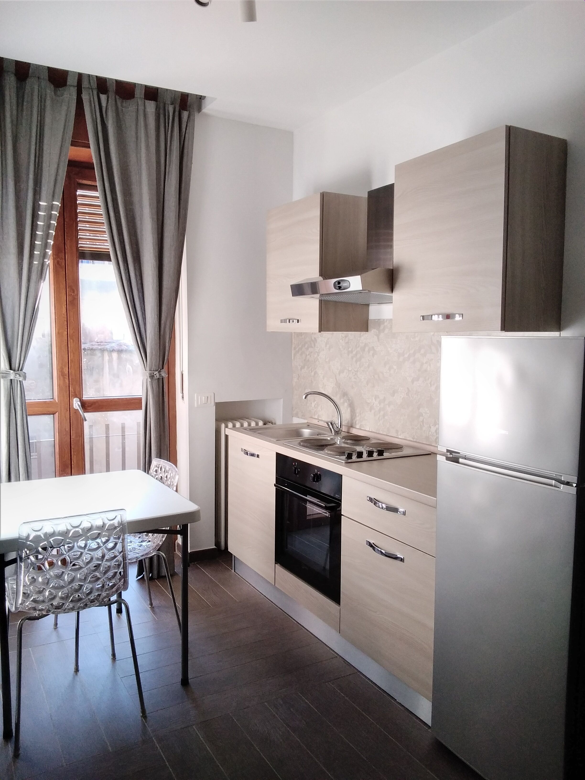 A modern kitchen with a built-in oven, a stainless steel refrigerator, and a wooden dining table with chairs.