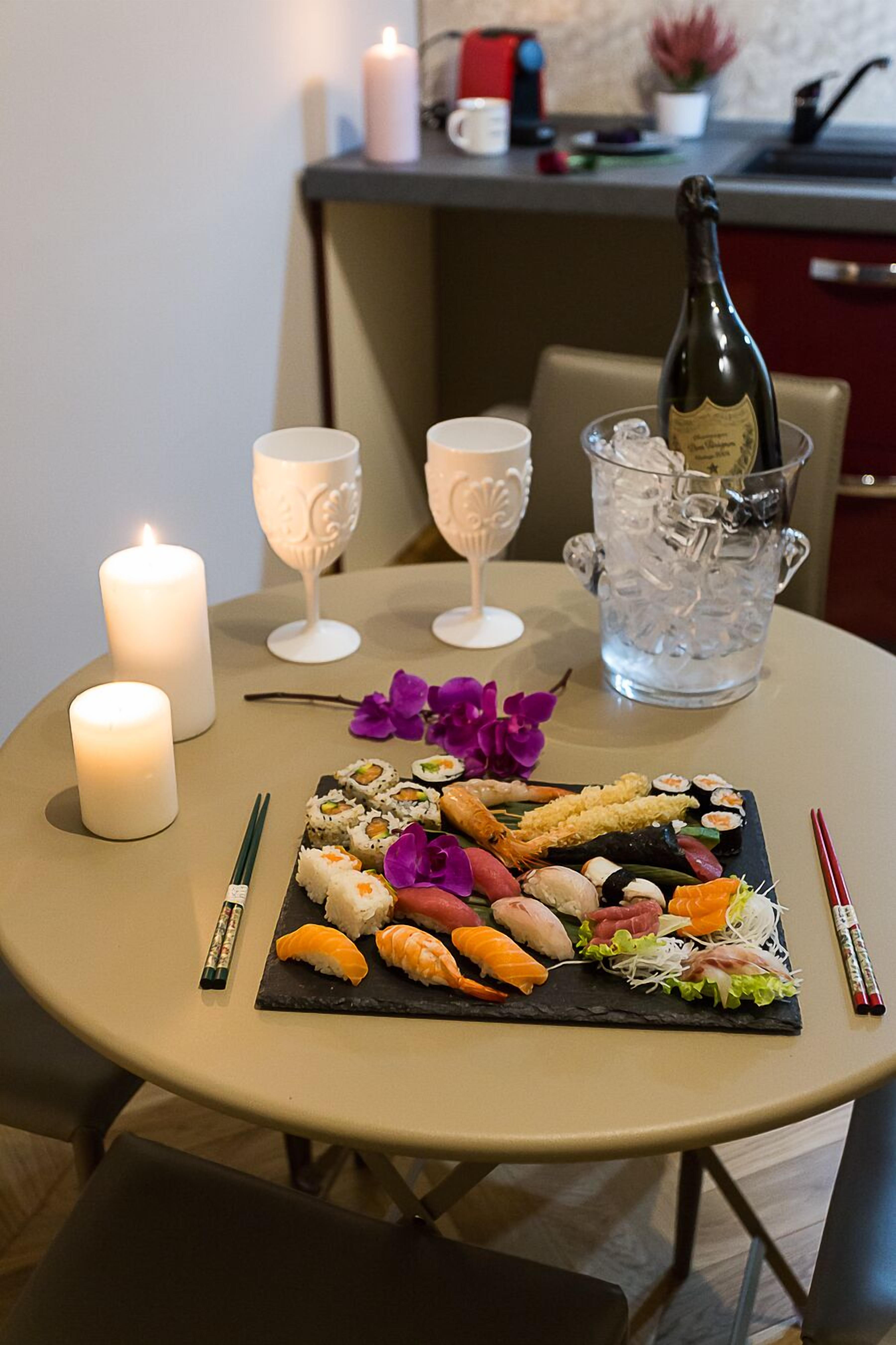 Une table de salle à manger ronde, sur laquelle on trouve un plateau de sushis, des bougies et une bouteille de champagne.