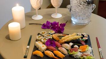 Une table de salle à manger ronde, sur laquelle on trouve un plateau de sushis, des bougies et une bouteille de champagne.