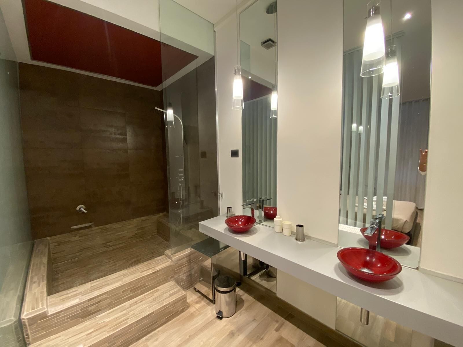 A modern bathroom with a glass-enclosed shower, a white vanity with a red bowl sink, and a large mirror.