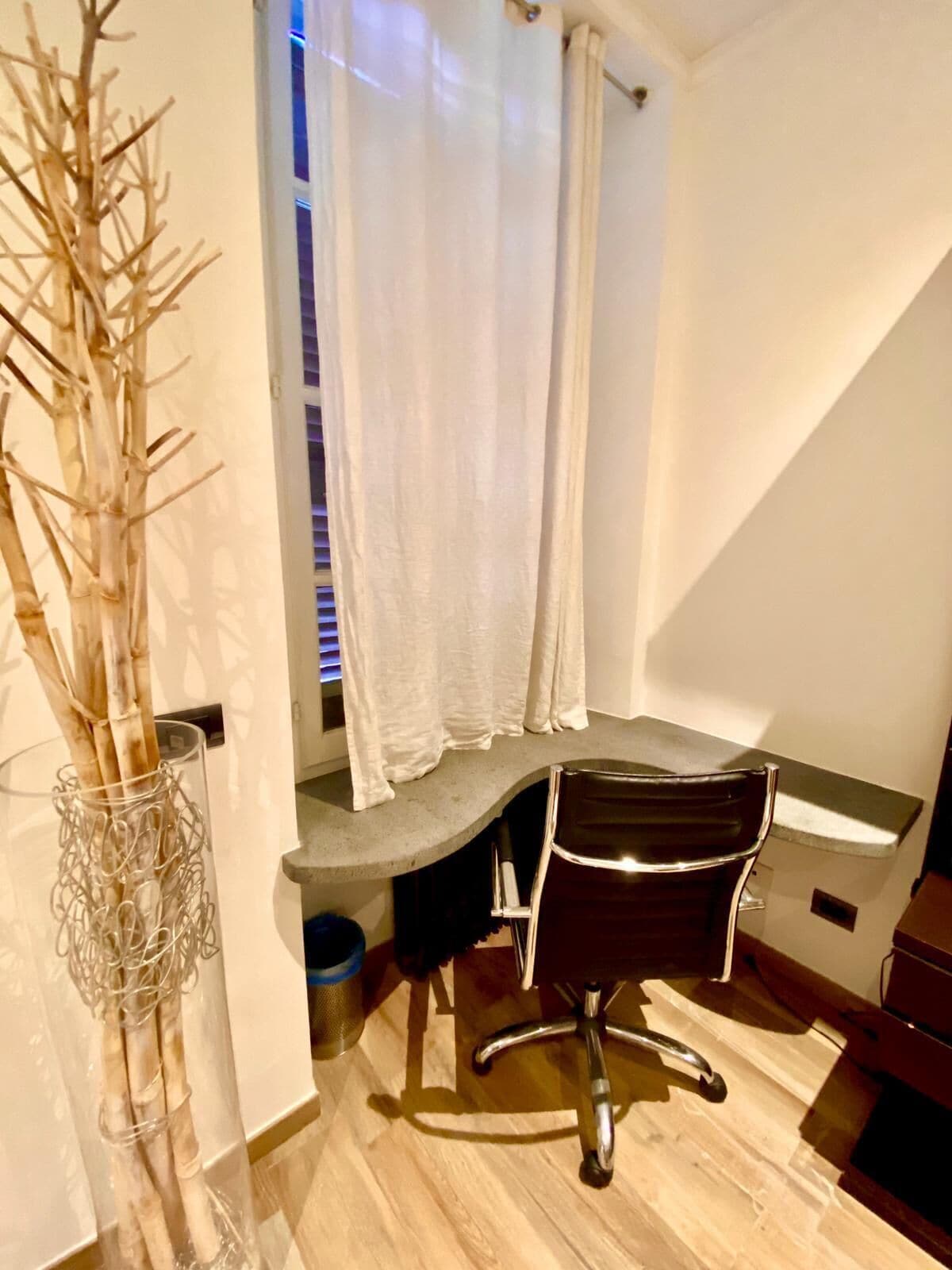 A small office space with a desk, chair, and a plant in a glass vase.